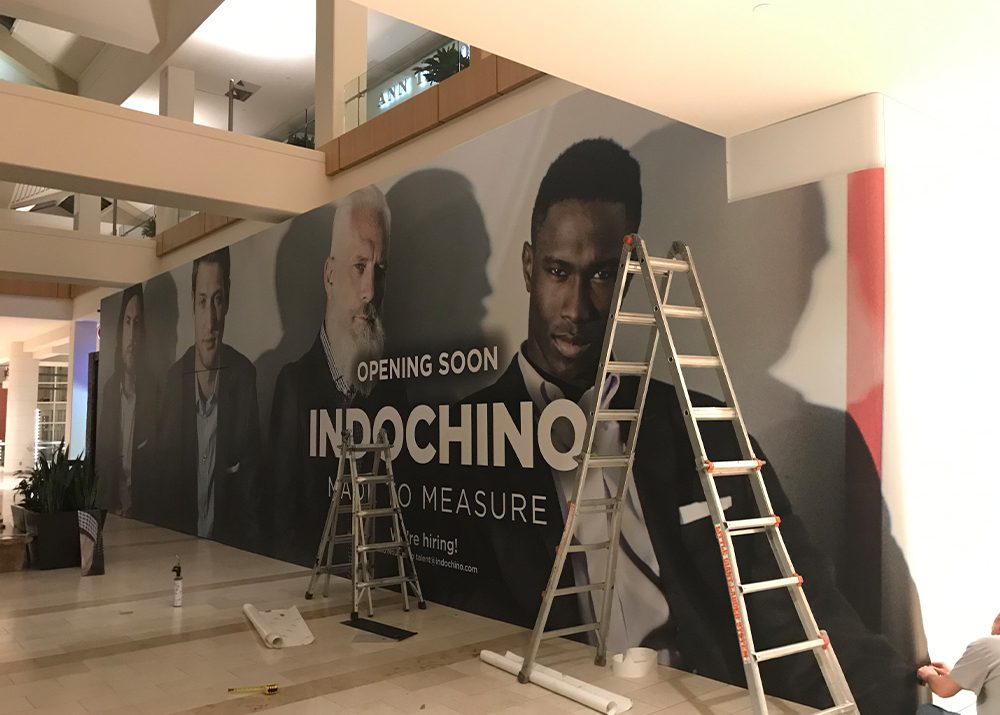 progress of wall wrap installation showing that a retail store in a shopping mall is opening soon behind a ladder